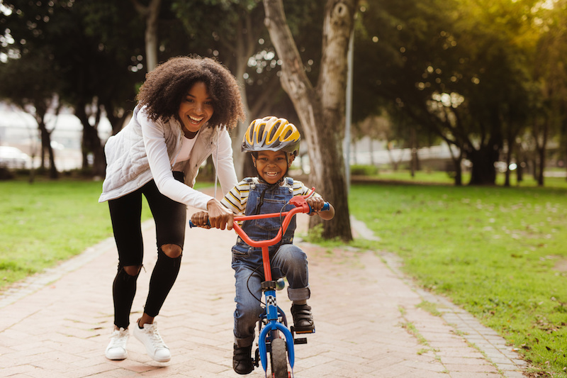 Little boy riding bike with help from his mom