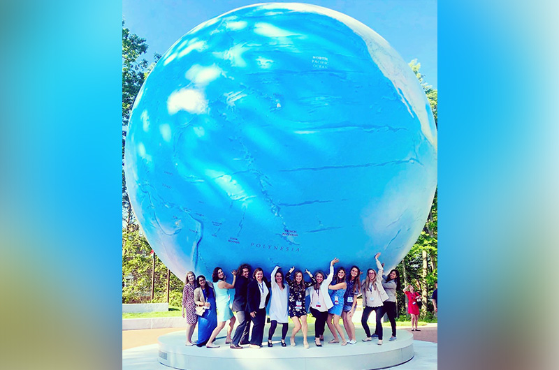 Attendees of the Female Athlete Conference pose beneath an enormous statue of the globe.