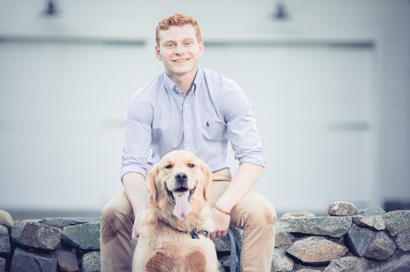 Jack, who had surgery for an ateriovenous malformation, sits on a stone wall with his dog.