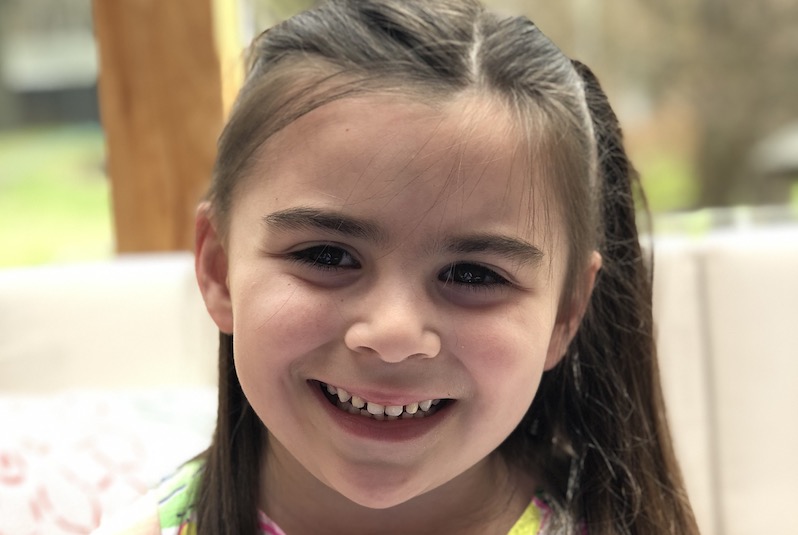 Grace, who had surgery for a cavernous malformation, smiles at the camera.