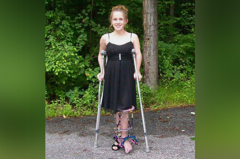 Lauren smiles for the camera, standing with crutches and an external device on her leg.