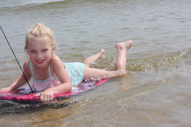 Elise, who has SYNGAP1, rides a boogey board at the beach.