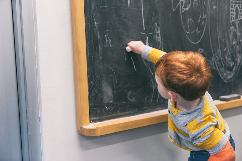 simon writes on a chalkboard with his hand that was affected by neonatal stroke