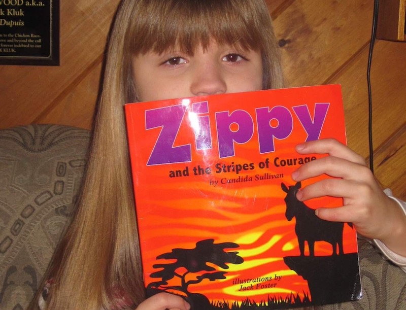 Maria, who was born with congenital scoliosis, poses with her book about a zebra named Zippy.