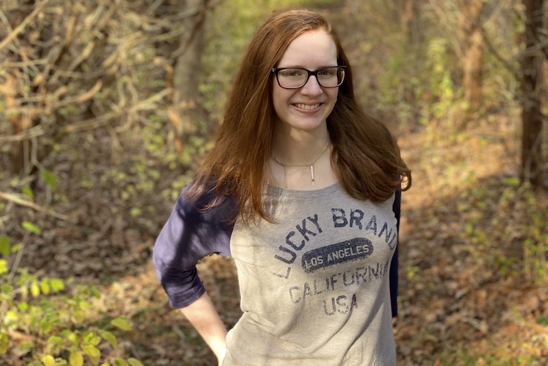 Ava, who has ACM, poses outside in the woods