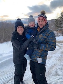 Emily and Leo outside with baby Olivia in ski clothes.