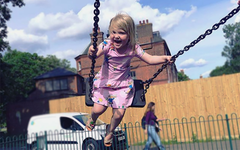 Poppy, who has SDS, swings outside on a swingset