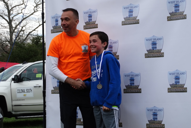 Will, who had an avulsion fracture in high school, wears a medal and shakes hands with his proud dad at an award ceremony.
