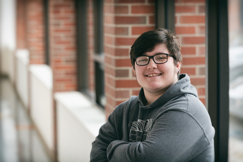 oliver, a trans teen, smiles with his arms crossed