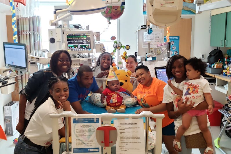 Kenny, a preemie who is in the ICU, on his bed, surrounded by his family, celebrating his first birthday
