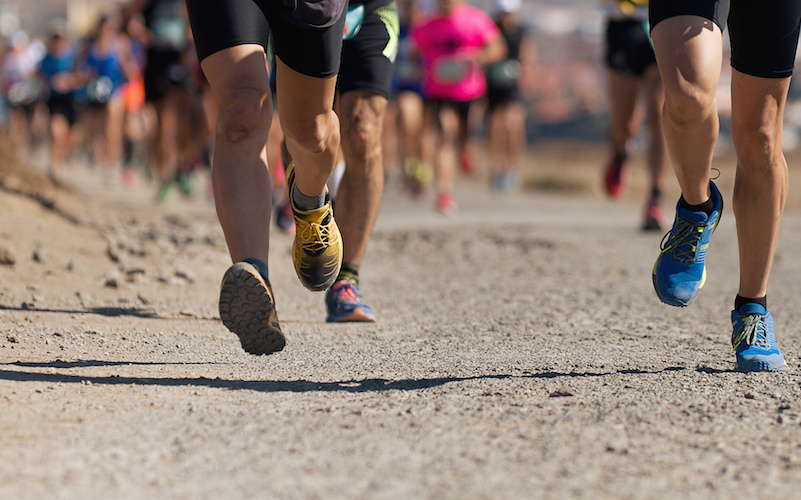 Closeup of legs and feet running on a dirt trail.