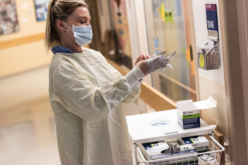 A woman in a hospital gown and face mask puts on gloves at Boston Children's during the COVID-19 outbreak.