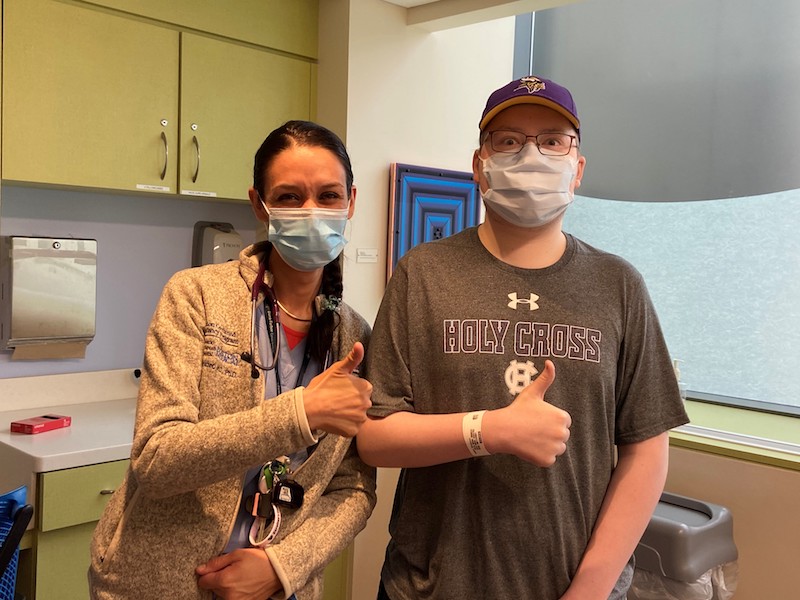 Young man who had ALL and his provider, both wearing masks, give the thumbs up sign