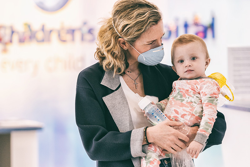 Mom with a mask holds a baby in a health care setting during the coronavirus