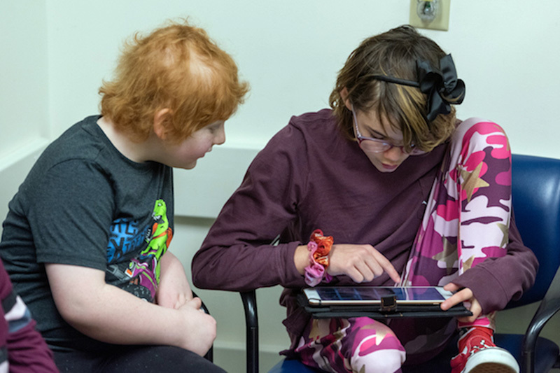 Rhys and Natasha play a game on an iPad. The two had limb-salvage surgery as part of their treatment for bone cancer.