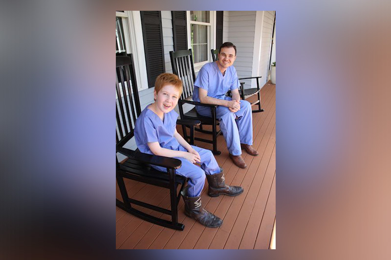 Spine surgeon Grant Hogue and Henry sitting in rocking chairs in scrubs and cowboy boots.