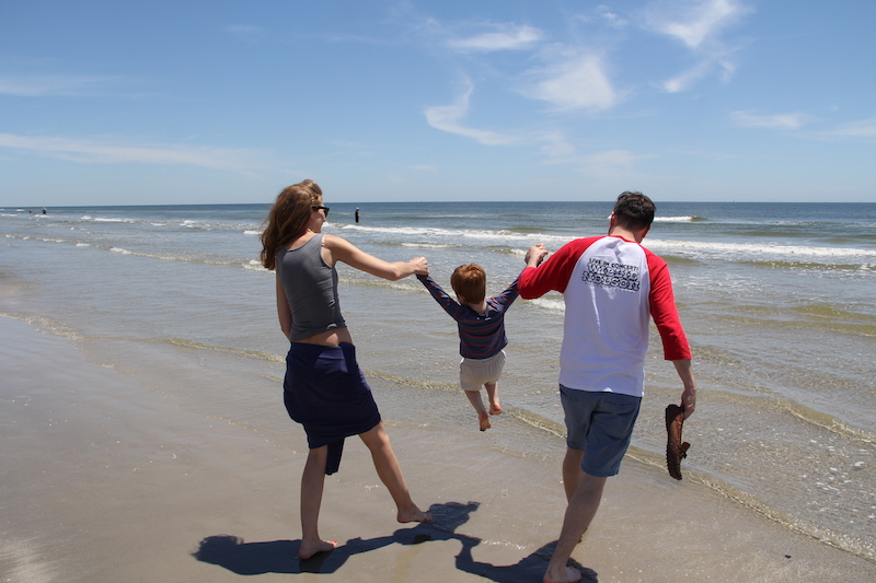 Megan and spine surgeon, Grant Hogue, swing young Henry by the arms over the surf.