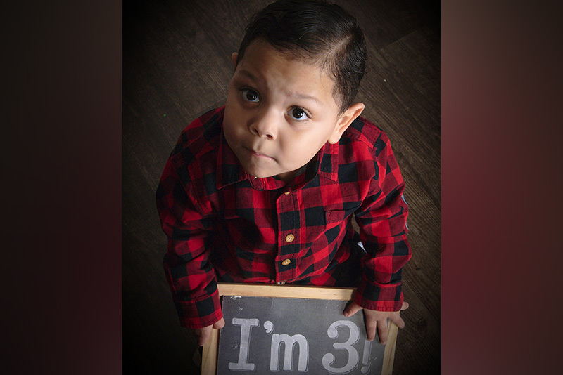 Gabby, who has short bowel syndrome, holds a chalkboard that reads "I'm 3!"