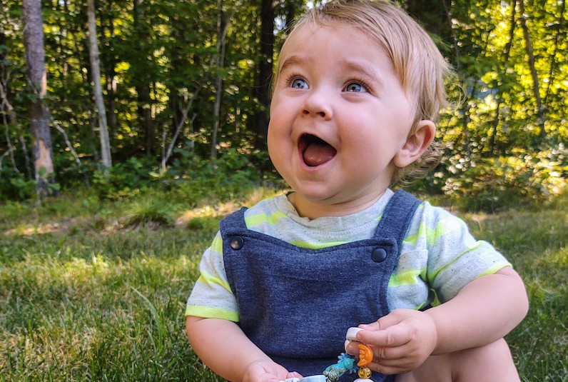 Nathan, who has OMS and an adrenal gland tumor, sits outside on the grass.