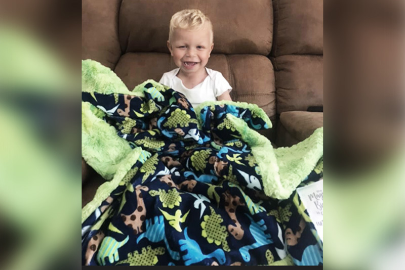 Rylan, who had a laryngeal cleft, cuddles under a blanket with dinosaurs on it.