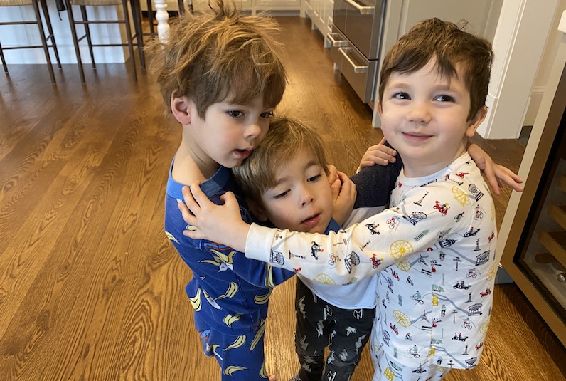 Three boys hug in their pajamas in a kitchen. Two had open heart surgery.