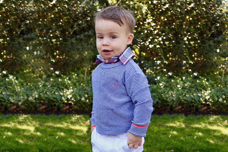 Tyler, who had a laryngeal cleft, stands outside. He is wearing a blue striped shirt.