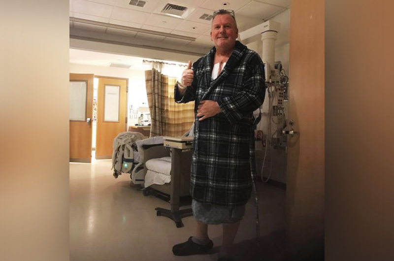 Jack Sr. stands in his hospital room wearing a bathrobe after surgery for his rare heart condition. He is giving a thumbs up sign.
