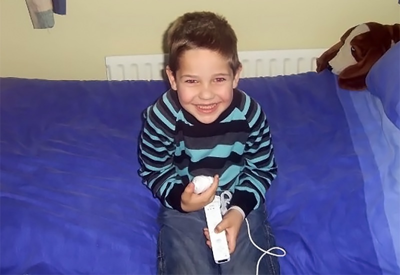 Marc, who had ALD, sits on a bed smiling.