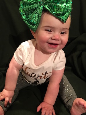 Harper, who was born with brachial plexus birth injury as an infant, wearing a large green bow on her head.